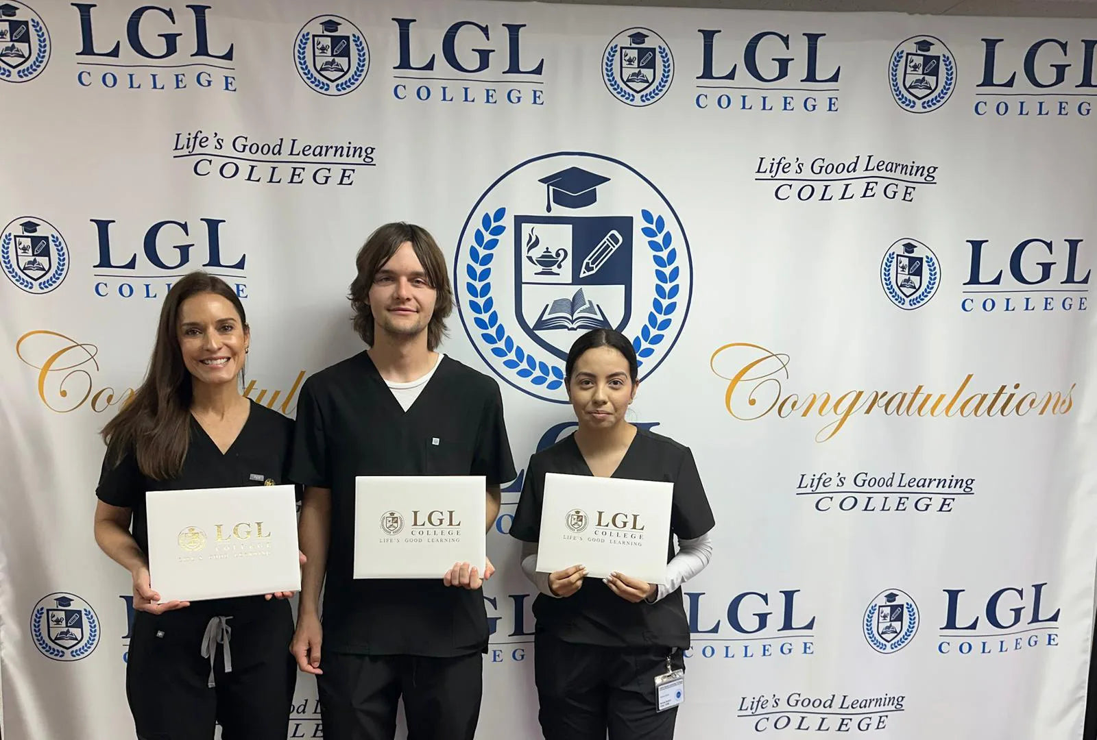 Three people in black scrubs hold certificates against a backdrop with the LGL College logo and the words 